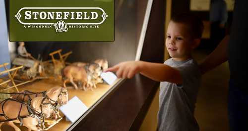 Wisconsin-Historical Museum. A large group of students and chaperones wearing matching shirts animatedly engage with a speaker off camera. Several girls raise their hands high!
